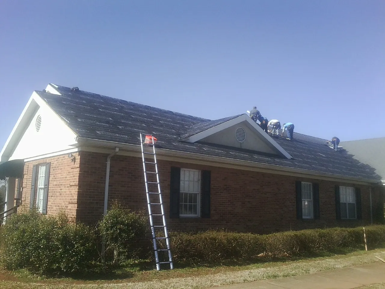 Crew tearing shingles off a brick ranch roof with a ladder set — Metal Roof Repair work by our crew in South Park