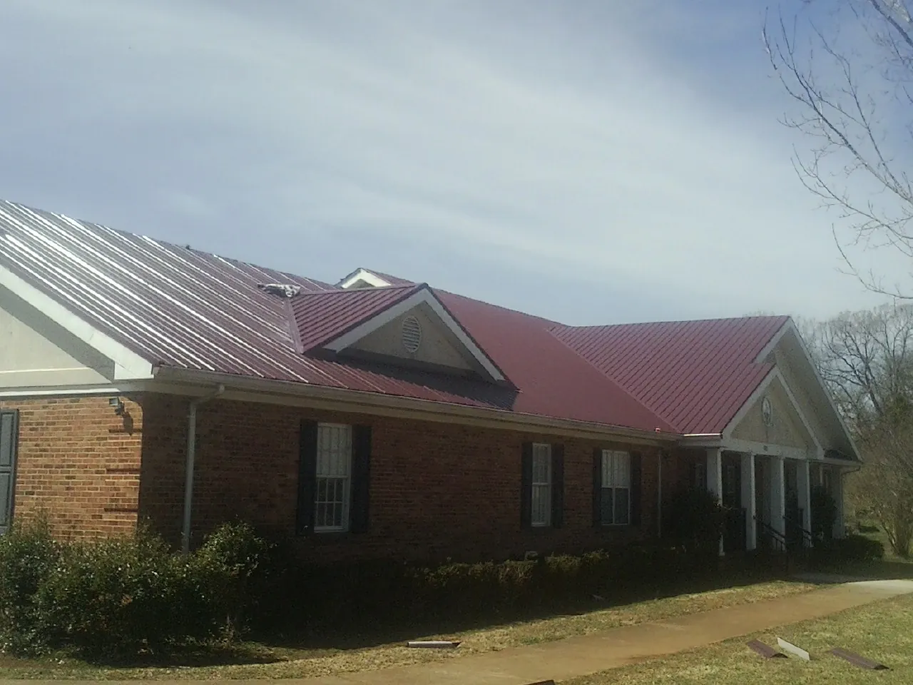 Red metal roof with gabled entries on a long brick building, from a Hail Damage Roof Repair job in South Park