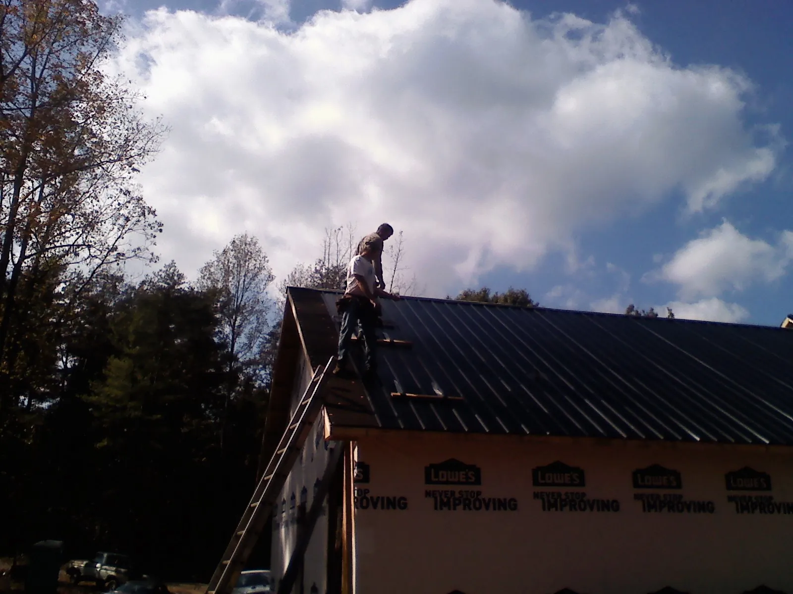 Roofer fastening dark metal panels high against a cloudy sky, from a Roof Inspection job in South Park