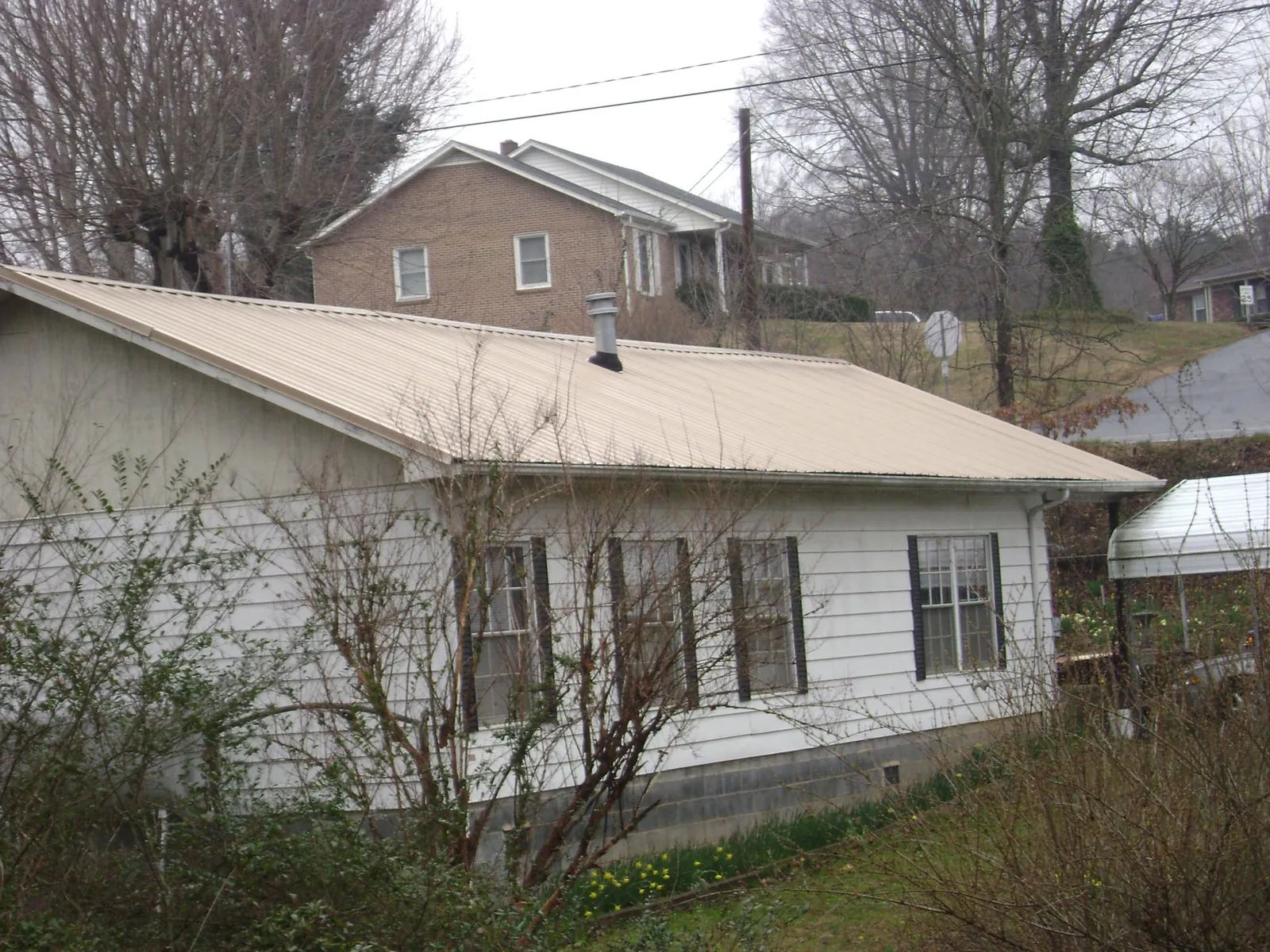 Tan metal roof on a white sided house set into a hillside — Commercial Roofing by Roofing Brothers in South Park