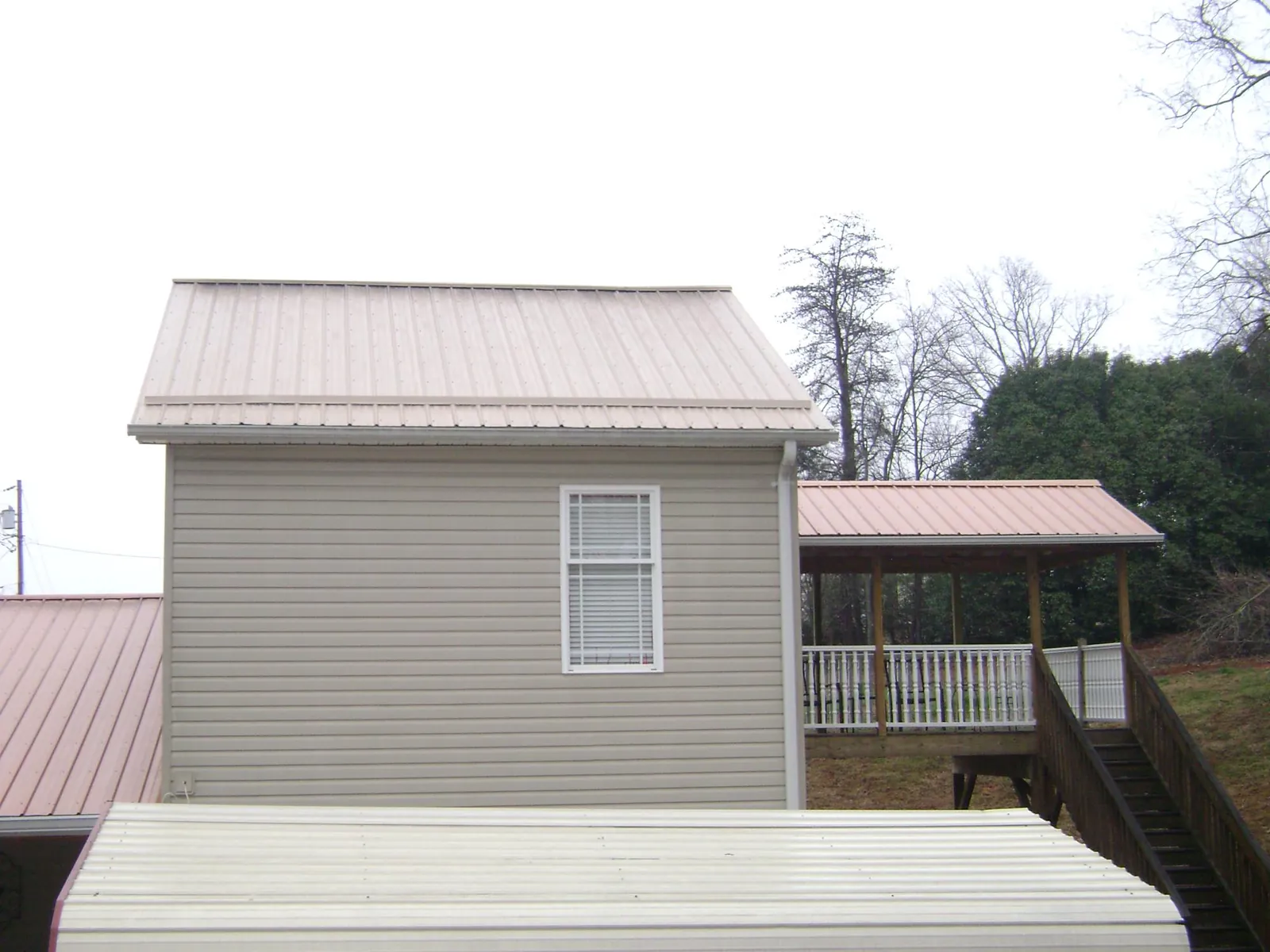 Tan metal roofs on a two story addition and attached porch, from a Roof Replacement job in South Park